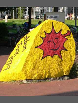 Foto eines Gedenksteins an Gorleben-Treck von 1979 mit roter AntiAtom-Sonne auf gelbe,m Grund