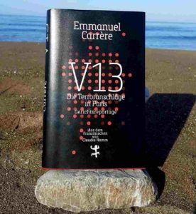 Buch V 13 (schwarzer Hinterfgrund, weiße Schrift) fotografiert am Strand vor Meer